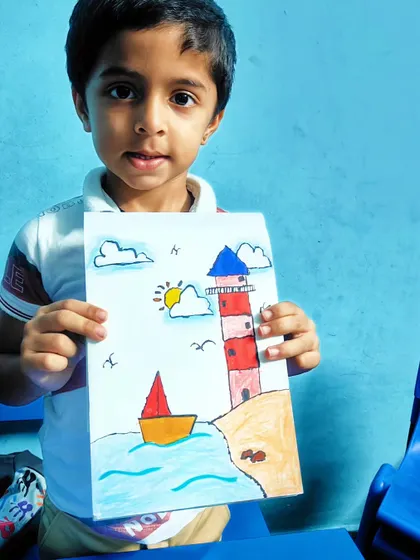 A young artist proudly holds his drawing of a lighthouse and sailboat, a classic seaside scene.