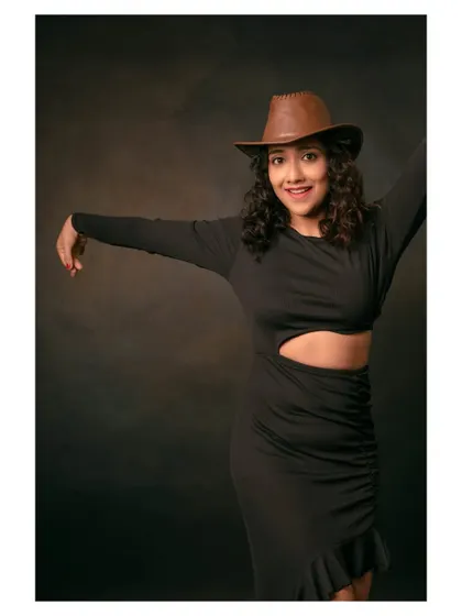 A playful and energetic portrait of a model in a black dress and cowboy hat. Her pose captures a moment of dance and celebration.