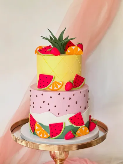 A fun and fruity two-tiered "Two-tti Frutti" cake. The bottom tier looks like a watermelon and the top like a pineapple, decorated with fondant fruit slices.