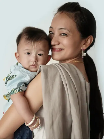 A mother holds her baby over her shoulder, sharing a quiet, loving moment. The soft, neutral tones create a calm and gentle mood.