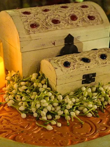 A close-up of the decor elements, including hand-carved chests and candles surrounded by fresh mogra buds, adding to the fragrant and visually rich atmosphere.
