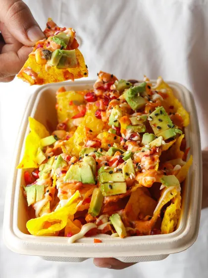 An action shot of a hand holding a loaded wonton nacho. This dynamic image makes the food feel interactive and delicious, encouraging customers to try this unique fusion dish.