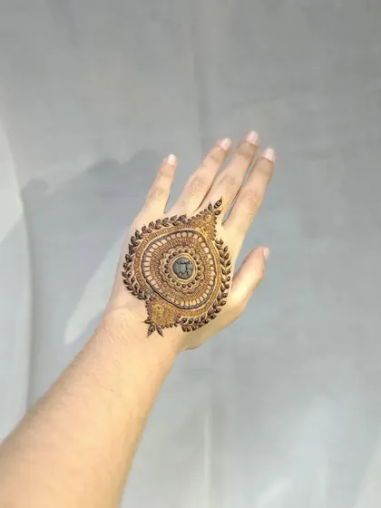 A bold mandala design on the back of the hand, framed with a border of leaves. The center is left open for the dark stain to create a powerful contrast.