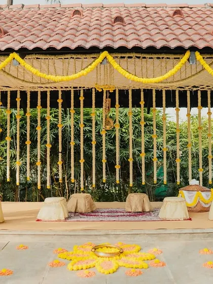 An eco-friendly Haldi ceremony setup under a rustic tiled roof, using traditional elements like jasmine and marigold flower strings and low seating for a truly authentic experience.