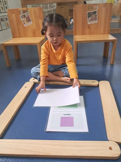 This girl is learning about shapes by building a frame around a picture card. It's a tangible way to understand geometric concepts and spatial relationships.