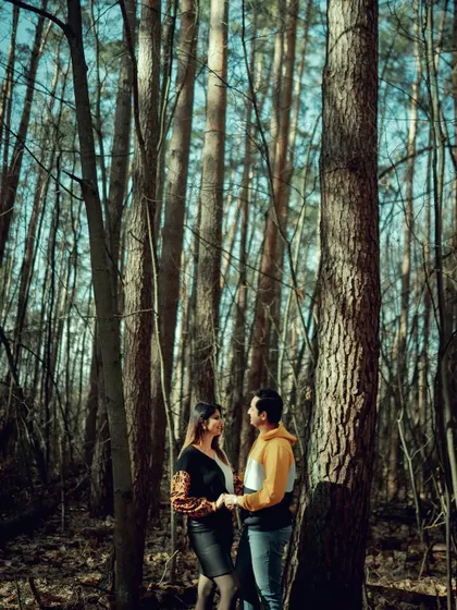 A romantic portrait of a couple standing close together in a sun-dappled forest in Germany. The tall trees create a beautiful, natural frame for their intimate moment.