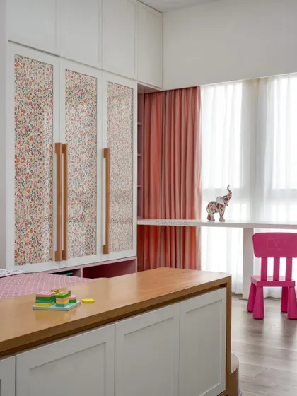 The wardrobe in the 'Cover me in Sunshine' daughter's room features beautiful fabric-sandwiched shutters and custom wooden handles. A small study desk by the window provides a bright spot for creative activities.