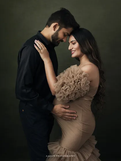 An elegant fine art maternity portrait of a couple, showcasing a classic, painterly style against a dark, textured backdrop. The focus is on their connection and the beautiful anticipation of new life.