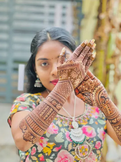 A portrait of a happy client, her face partially hidden by her beautifully stained mehendi hands.