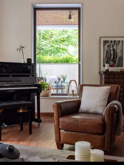 A symphony of comfort and character. This corner features an elegant black piano next to a vintage leather armchair, creating a sophisticated retreat for music and relaxation, complemented by fresh florals and curated art.