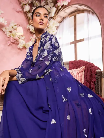 A seated portrait in a deep blue ensemble. The makeup is elegant and understated, with a focus on a flawless complexion and softly defined eyes.