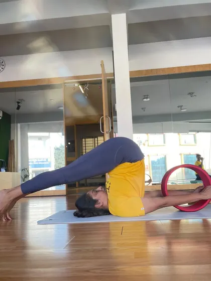 A student transitions into Halasana (Plow Pose) from a shoulder stand on the wheel, demonstrating flexibility and control.