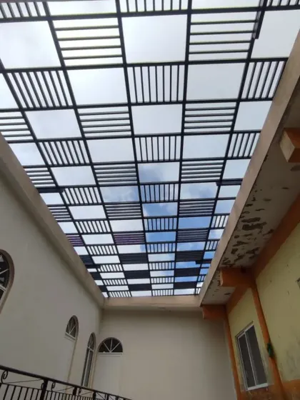A view from below a complex rafter and polycarbonate roof during installation. The grid-like pattern creates a modern, industrial aesthetic while providing both shade and light.