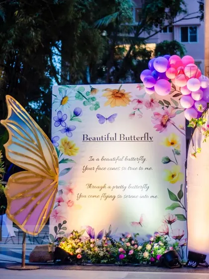 A whimsical photo opportunity at a butterfly-themed party. A large, beautifully decorated butterfly wing stands next to a floral backdrop, allowing guests to take magical photos.