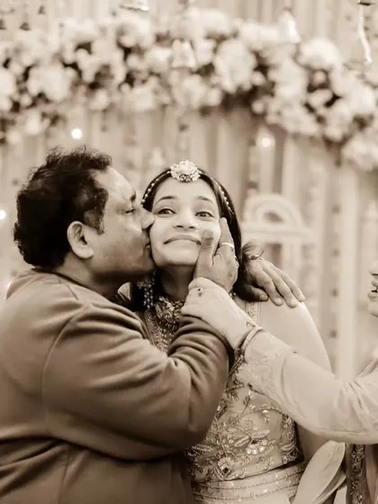 A priceless family moment from a Haldi ceremony. The bride is showered with kisses from her mother and father, her happy face at the center of their love.