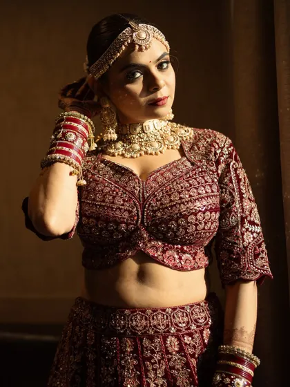 A powerful portrait of the bride in her deep red velvet lehenga. The dramatic lighting highlights her sculpted features and the rich texture of her outfit.