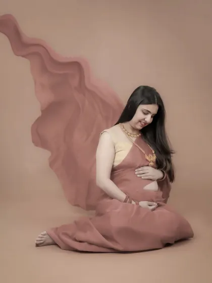 A quiet and artistic fine art portrait. This mom-to-be is seated, looking down at her bump, with the fabric of her gown flowing beautifully around her.