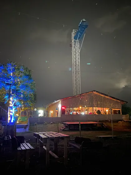 The vibe at our venue after dark. This shot captures our cozy cafe area and the towering bungee jumping platform lit up against the night sky, showcasing the blend of chill hangout spots and high-adrenaline adventure we offer.