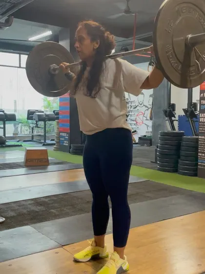 A female athlete holding the bar in the starting position for a drop snatch. This drill improves shoulder stability and reinforces a solid catch position.