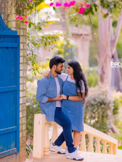 A romantic moment on a balcony, framed by a bright blue door. The couple's matching denim outfits create a coordinated and stylish look.