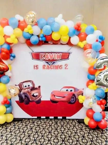 A "Racing 2" birthday party featuring characters from Disney's Cars. I use a custom printed backdrop with Lightning McQueen and Mater, framed by a colorful balloon arch, and a silver foil number '2' balloon.