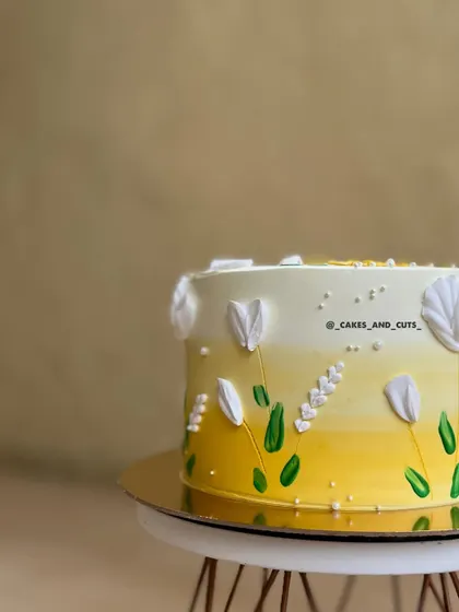 A close-up of a cake with a yellow ombre effect and hand-painted floral details. We explore color blending and painting on buttercream in our classes.