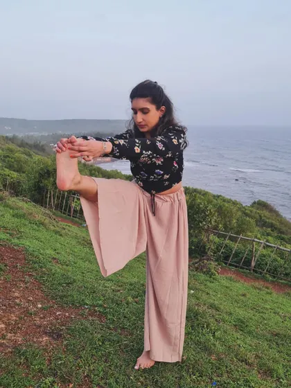 Practicing a standing leg stretch on a cliff overlooking the sea. This pose, an extension of the leg, challenges balance and improves flexibility in the hamstrings.