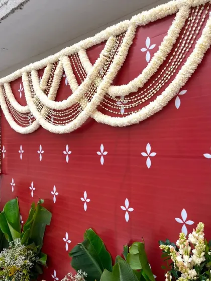 A classic South Indian decor element. This backdrop features a deep red wall with delicate Kolam patterns and a beautiful valance made of jasmine strings (Moggu Jade).