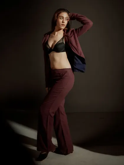 A full-length studio shot demonstrating how lighting can define a space. The sliver of light on the floor grounds the model, drawing attention to her confident stance and the flow of the wide-leg trousers.