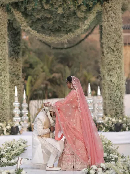 A tender moment of love and respect during the Varmala ceremony, framed by a lush floral arch. We focus on creating a serene and beautiful setting for these sacred traditions.