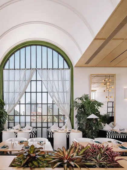 Looking out through the grand arched window at Brassa, which floods the dining area with natural light. The design incorporates abundant greenery, blurring the line between the indoor and outdoor spaces.