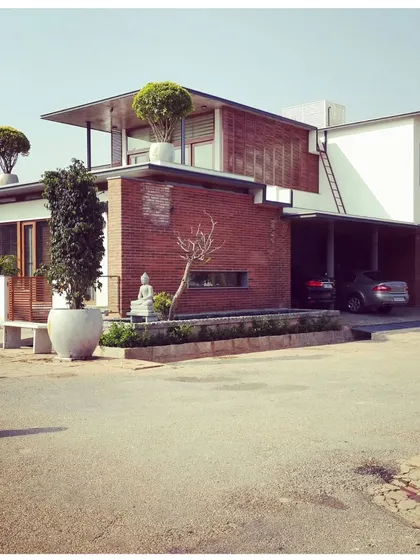 This Bengaluru residence showcases a blend of modern forms with natural materials like brick and wood. The design incorporates cantilevered roofs and large planters, integrating the building with its landscape.
