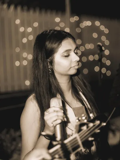 A close-up, black-and-white portrait of a singer performing at an intimate gathering. This artistic choice emphasizes her focused expression and the emotional mood of the music.
