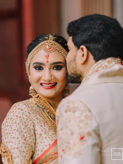 A sweet kiss on the cheek, a candid moment filled with affection. The bride's happy glance towards the camera makes this an endearing memory from their South Indian wedding reception.
