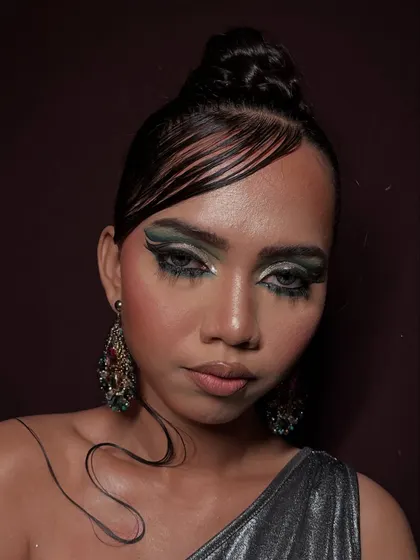A high-fashion look with a wet, glossy finish. The dramatic green and black eye makeup is paired with sculpted, slicked-down hair to create a modern and edgy vibe for this editorial photoshoot.