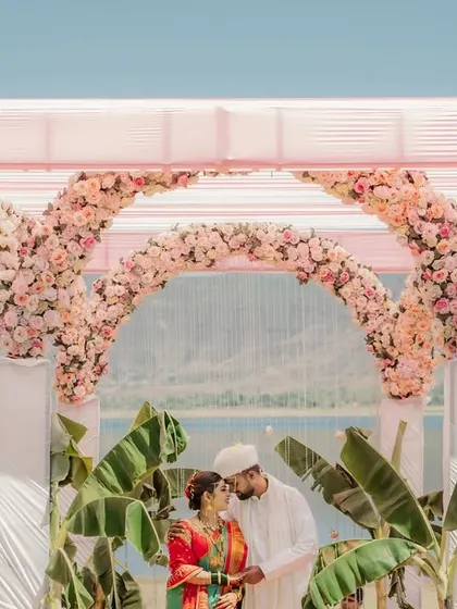 A tender kiss on the forehead under a beautiful floral arch. This Maharashtrian wedding by the water is the picture of romance.