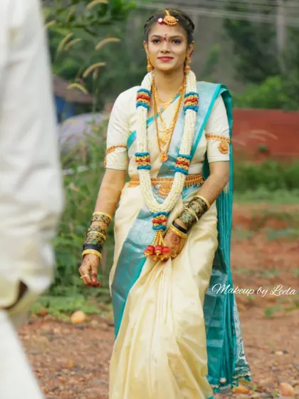A radiant South Indian bride ready for her Muhurtham. This look features classic makeup that enhances her natural beauty, paired with a traditional off-white and teal silk saree and authentic temple jewelry.