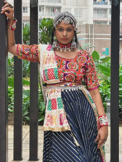 This pose shows the complete outfit, from the detailed blouse and jewelry to the flowing, multi-patterned skirt.