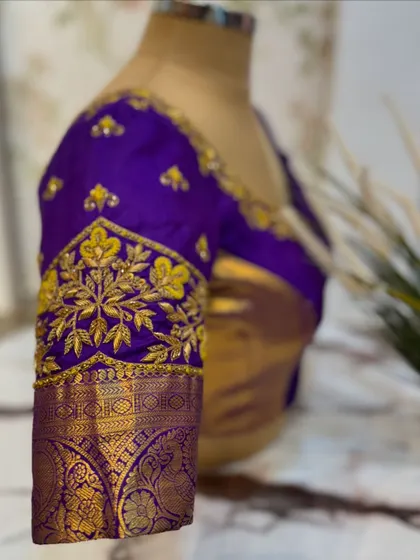 A close-up of the sleeve of the purple blouse, highlighting the intricate floral embroidery and zari work.