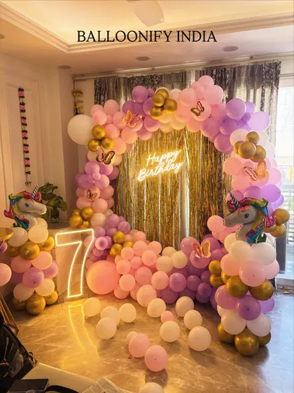 We brought a unicorn dream to life for this 7th birthday party. This popular theme features a circular balloon arch in pastel pink, purple, and gold, a 'Happy Birthday' neon sign, and a large light-up number '7'. The unicorn balloon pillars on each side complete the magical look.