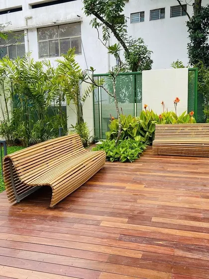 This image showcases the beautiful wooden deck we installed, complemented by modern, sculptural benches. The combination of natural wood and surrounding greenery creates a warm and inviting outdoor seating area.