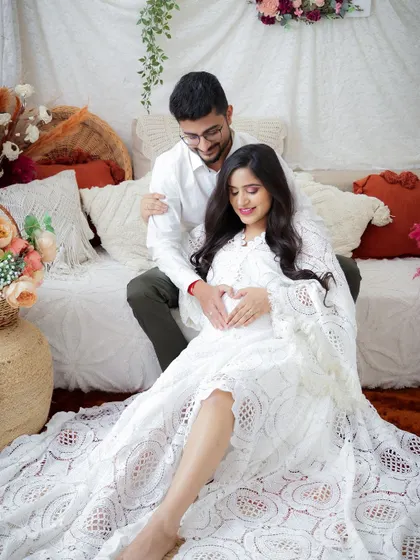 A cozy and intimate portrait of a couple in a boho-styled setup. Their hands forming a heart on the baby bump is a beautiful symbol of their growing family.