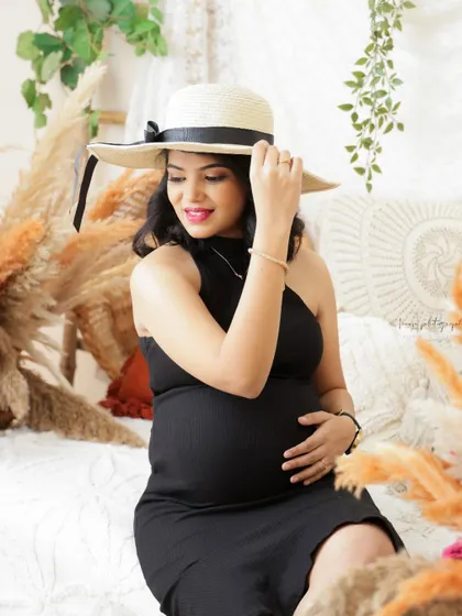 A chic and stylish portrait in a boho setting. The mom-to-be wears a simple black dress and a sun hat, creating a sophisticated look.