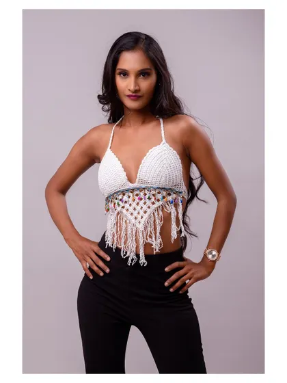 A strong and confident studio portrait of a model in a white crochet top. The pose is powerful, highlighting her physique and the details of the outfit.