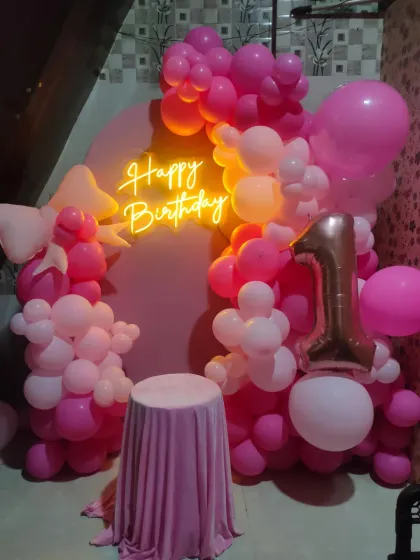 The same pink arch backdrop, now with a neon sign and a small table for the cake, showing its versatility.