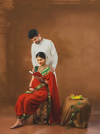 A quiet, loving moment from a traditional maternity session. The couple is dressed in ethnic wear, with the mom-to-be reading a book while her partner stands lovingly behind her.