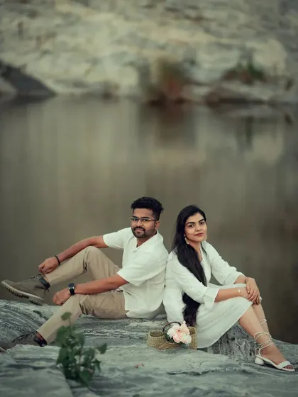 A serene pre-wedding portrait of a couple sitting back-to-back by the water, creating a balanced and peaceful composition.