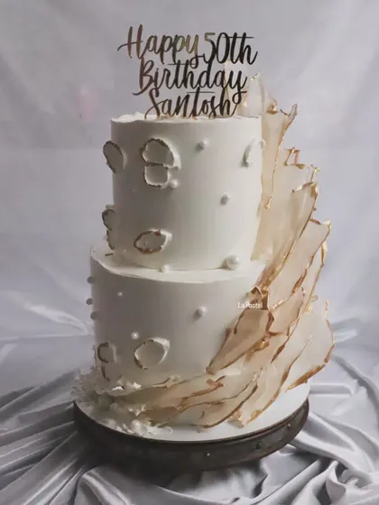 A grand two-tier cake perfect for a 50th birthday or anniversary. The design features abstract golden sails and delicate pearl details, creating a modern and artistic statement piece.