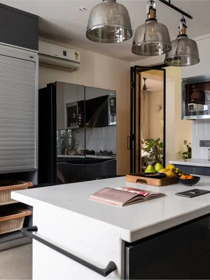 This perspective showcases the smart storage solutions, including a tall unit with built-in ovens, a rolling shutter for appliances, and pull-out wicker baskets. The glossy grey cabinets add a sleek, modern touch.