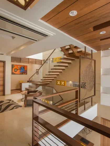 A view from the upper level of Kavyam Residence shows how the wooden staircase links the floors to the double-height living area. A skylight above ensures that natural light filters through all levels of the home.